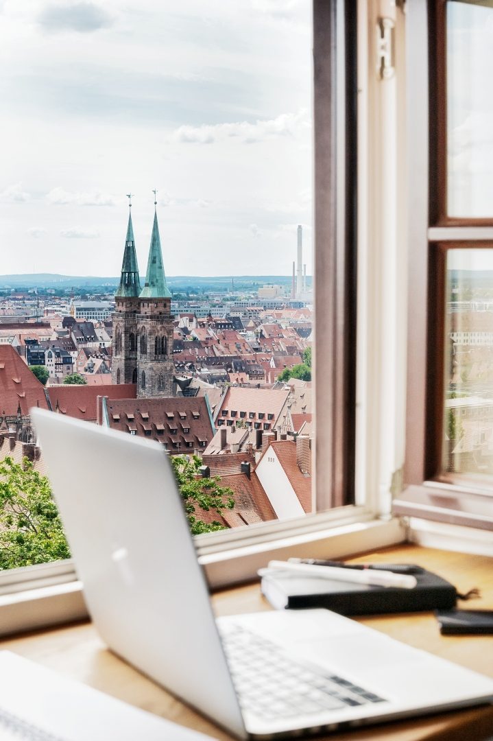 Arbeiten mit bester Aussicht: Vor einem Fenster steht ein Laptop auf einem Tisch, draußen ist die Stadt Nürnberg zu sehen.