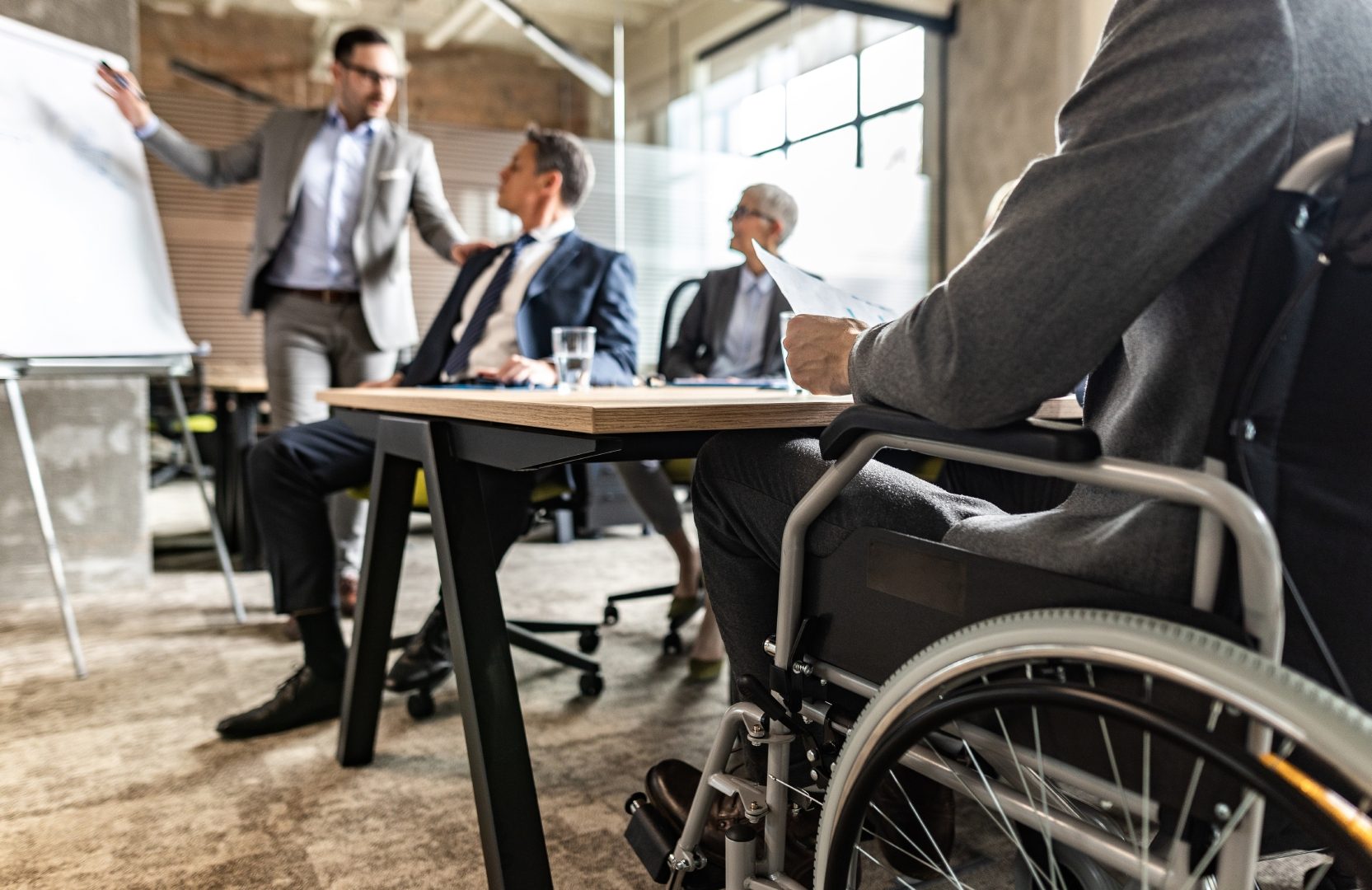 Flexibilität und New Work: Ein Geschäftsmann, der in einem Rollstuhl sitzt, ist bei einem Meeting mit weiteren Personen im Büro.