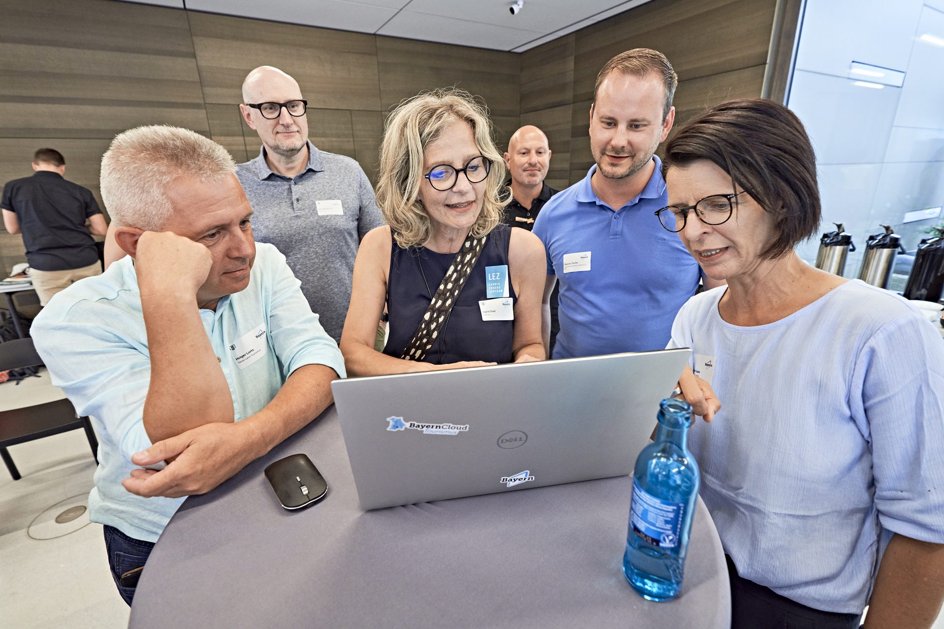 3 Männer und 2 Frauen schauen gemeinsam bei einem Netzwerk-Event in einen Laptop, der auf einem Tisch steht